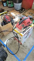 Two Skil sanders and Wagner Power Roller paint sprayer on a floor with some paint cans and tools in background