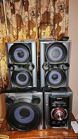 Front view of 3-piece speaker system including two identical standing speakers with dual drivers and one larger subwoofer speaker, all with blue speaker cones.