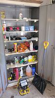 Full view of open metal cabinet showing shelves with automotive products, tools, fluids, and shovel