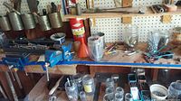 Wide view of the workbench showing attached vises, jars with hardware, a funnel, sockets, wire brushes, and other tools spread out.