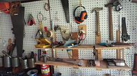 Wide view of pegboard wall displaying various hand tools such as hammers, saws, brushes, files, measuring tapes, and rolls of metal bands.