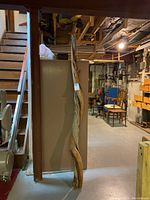 Full view of the twisted wooden post standing upright in basement setting, showing its full height and rough texture.
