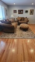 Full view of the beige floral patterned Shaw area rug placed under a living room set on hardwood flooring.