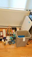 View of wooden easel, white file folders, plastic bin, and various smaller art supplies arranged on floor