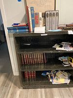 Bookshelf showing top shelf assorted books, middle shelf religious volumes, bottom shelf miscellaneous papers