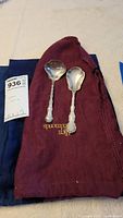 Two Gorham sterling silver serving spoons placed on burgundy cloth with MaxSold tag
