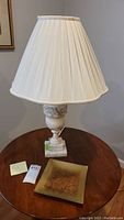 Full view of marble effect table lamp with white pleated shade and square base, accompanied by the decorative glass plate on a wood circular table.