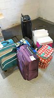 Lot setup showing all suitcases, coolers and backpacks in corner on concrete floor.