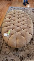 Full top view of the oblong tufted ottoman showing light brown fabric upholstery and button tufting.