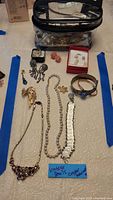 Clear photo showing assortment of necklaces, bracelets, earrings, and brooches spread out on a table, with a note indicating 'Vintage Pearls' and packaging bag with more jewelry inside
