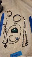 Overview of sterling silver jewelry lot on cream fabric, including bracelets, necklaces, pin, and ring