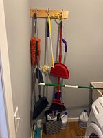 Photo of hanging cleaning tools including brooms, dusters, dustpan, and mop bucket with bleach bottles on floor