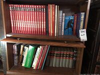 Full view of wooden bookshelf with two shelves filled with various books, featuring Popular Mechanics bound volumes and other assorted books on different subjects.
