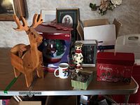 Overall view of the snow globe in packaging, wooden reindeer plant holder, mugs, glassware, and Christmas decor on table