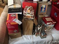 Multiple lighted Christmas village buildings on a couch with boxes. Includes a popcorn stand, houses, tree shop, and Christmas tree decorations.