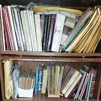 Top shelf of wooden bookcase with a variety of cookbooks and recipe booklets, including some in manila envelopes (not included).