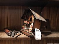 Photo showing the cuckoo clock side on with weights and pendulum detached and placed nearby on the shelf.