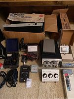 Wide view of assorted electronic and diagnostic equipment, including analog meters, signal generators, multimeter, and tool belt on carpet.