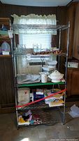 Full view of metal wire shelving unit with items stored on shelves including glassware, dishes, papers, and miscellaneous.