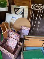 Overall lot showing floral storage boxes, wooden organizer, white metal plant stand, brown magazine rack and embossing sheet box.