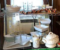 Shelf displaying colorful striped Tex Mex boot-shaped mugs, square and rectangular serving dishes, and Pampered Chef tiered server with ceramic bowls, plus glassware and serving utensils.