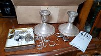 Overall shot showing pair of weighted sterling candlesticks on wooden surface alongside jewelry box with chains and loose rings and earrings