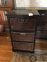 Front view of storage chest showing 3 wicker drawers with cut-out handles and dark wood frame. Visible wear on wicker and wood surfaces.