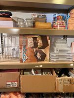 Three shelves on one shelving unit featuring craft supplies, storage bins in box, plastic drawers and miscellaneous items in cardboard boxes underneath
