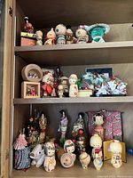 Three shelves displaying various wooden kokeshi dolls, cloth figurines, and paper origami items