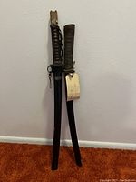 Two swords vertically leaning against wall with scabbards on