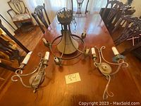 Photo showing one chandelier and two matching metal wall sconces on a wooden table. Each piece shaped with curved arms holding candle-style bulb sockets. Condition lightly used with some wear visible.