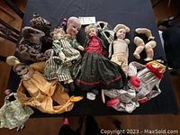 Lot of antique dolls and puppets including several dolls dressed in vintage clothes and multiple separate doll limbs, lying on a dark surface.