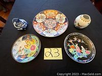 Board with lot number alongside three decorative plates and one small vase, all Asian style with painted designs.