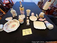 Photo showing a variety of porcelain items including plates, figurines, a lamp, vases, and small decorative objects on a table.