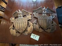 Two wooden logos featuring an eagle perched above a shield with stars and stripes, placed on a wood surface.