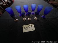 Full set of eight cobalt blue Murano glass cups with silver stands on a black tablecloth.