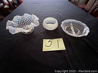 Three white hobnail glass pieces on black cloth: ruffled bowl, small round bowl, divided dish