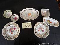 Complete view of all seven porcelain pierced plates and dishes including two large round plates, one oblong, and four smaller dishes in different shapes, all decorated with floral decals.