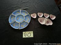Blue porcelain snack tray with six compartments and gold butterfly accents alongside eight small white heart-shaped porcelain dishes with pink floral designs arranged on a dark surface.