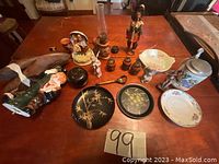 Full spread of all items on table showing porcelain figurines, plates, beer stein, wooden containers, music box, and oil lamp.