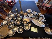 Photo showing the entire collection of silver-plated items spread out on a black table cloth, including various candle holders, trays, bowls, and pitcher, labeled with lot number 47.