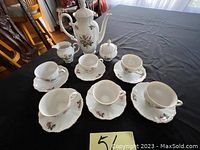 Full set including 6 tea cups and saucers, coffee pot, sugar bowl and creamer all with floral rose patterns and gold trim, arranged on a black cloth.
