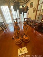 Front view of the two nude female figurine table lamps on a wooden table with furniture in background.