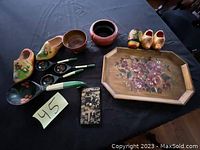 Photo showing the entire lot on black cloth background: two pairs of wooden shoes, three wooden spoons with painted handles, wooden bowl, round vessel, octagonal tray with floral design, matchbox holder with floral design.