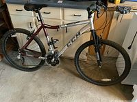 Full side view of CCM Equator bicycle showing the silver and maroon aluminum frame with CCM branding, black knobby tires, and front suspension fork.