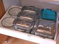 View of two stainless steel chafing dishes with glass pans and lids, one three-serving and one two-serving, plus two cut glass serving bowls and blue cloth items.