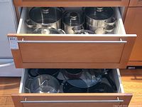Two open kitchen drawers showing assorted stainless steel cookware and lids