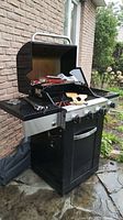 Open grill showing three main burners, cast iron grates and metal tools on the cooking surface