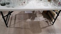 Side view of folding table showing resin top and black metal legs with adjustable height frame and folding mechanism.