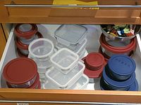 Top view of drawer showing glass food storage containers with various colored plastic lids and a bowl of bag clips.